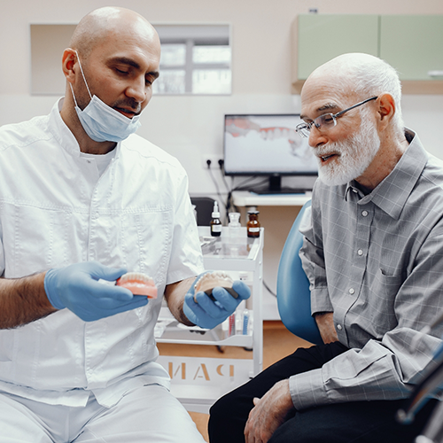 Dentist showing senior patient dentures and model of teeth