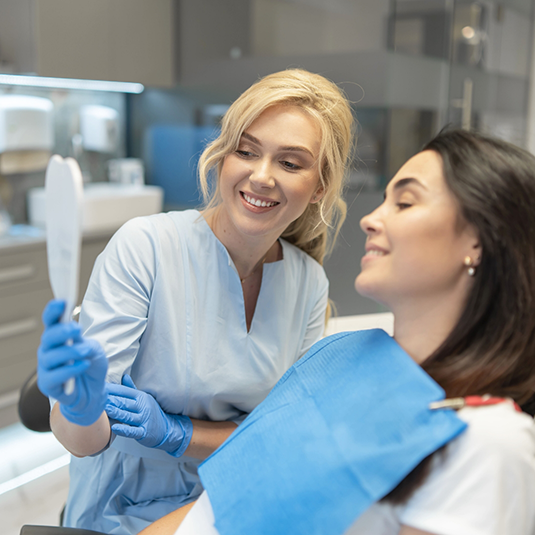 Blonde female dentist showing patient smile in mirror after cosmetic dentistry in Los Gatos