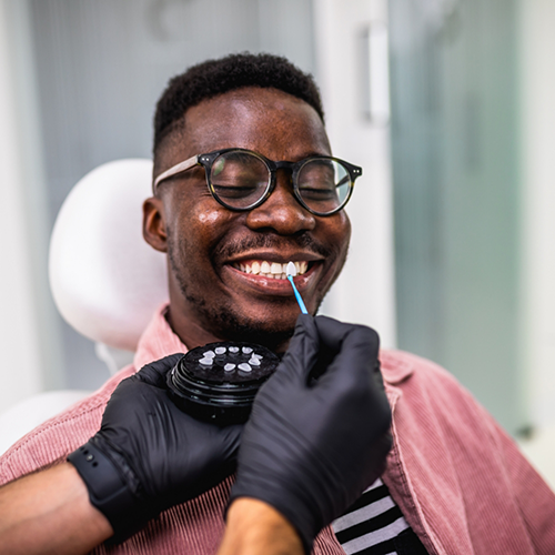 Man sitting in dental chair being shade-matched for veneers