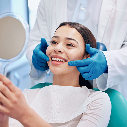 Woman sitting in dental chair smiling and holding handheld mirror