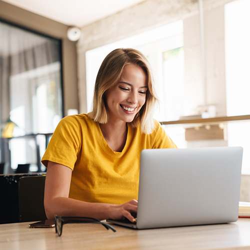 Woman in yellow shirt typing on laptop