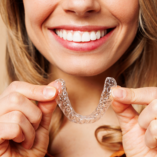 Close-up of smiling woman holding Invisalign clear aligners in Los Gatos