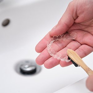 Patient using toothbrush to clean aligners in sink
