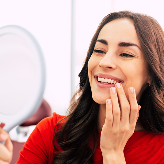 Woman in red shirt looking in mirror and smiling