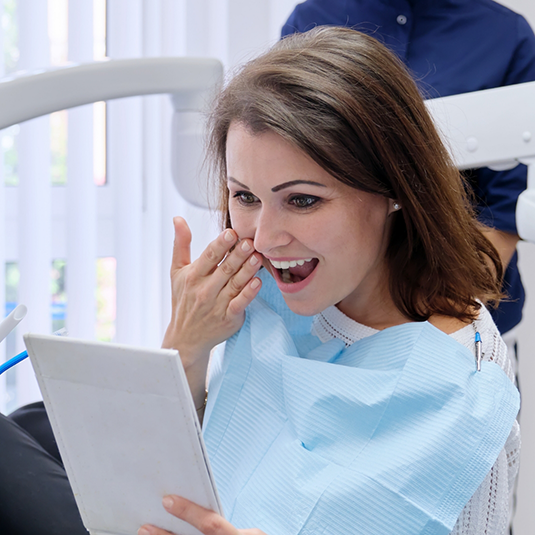 Smiling woman checking smile after restorative dentistry in Los Gatos